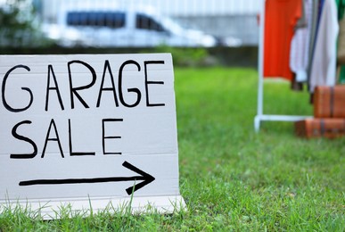 Sign Garage sale written on cardboard in yard. Space for text