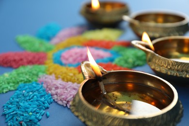 Diwali celebration. Diya lamps and colorful rangoli on blue background, closeup