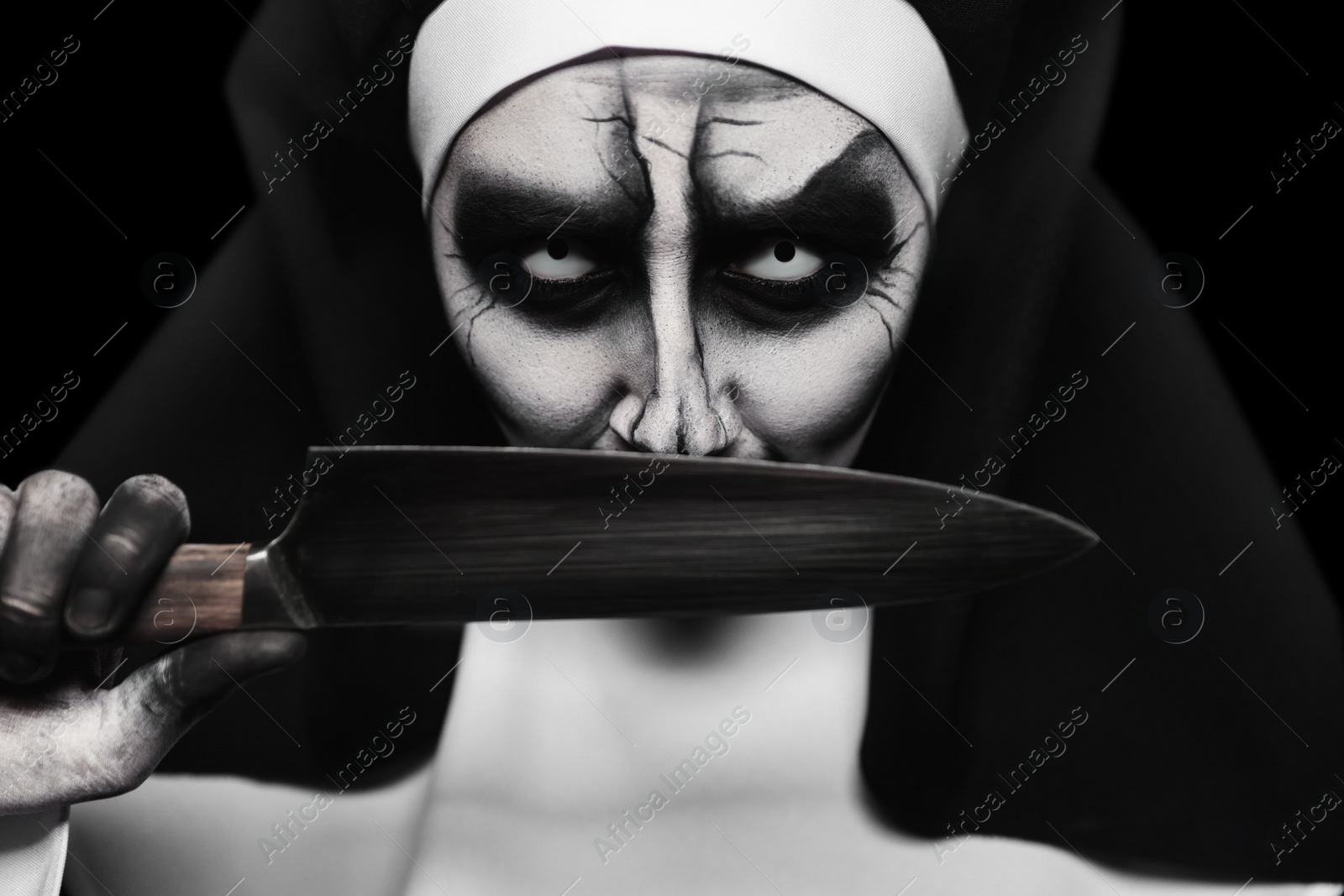 Photo of Scary devilish nun with knife on black background, closeup. Halloween party look