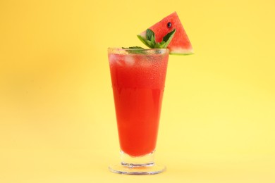 Photo of Delicious drink with mint, piece of fresh watermelon and ice cubes on yellow background