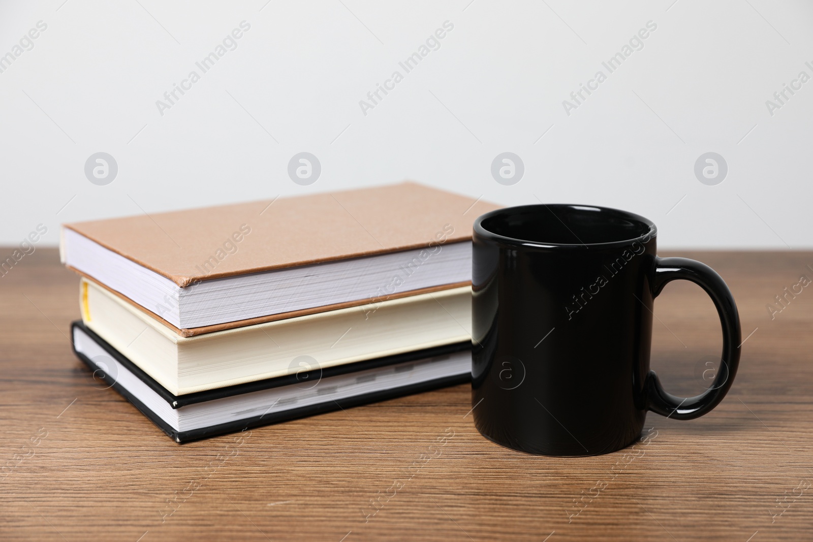 Black ceramic mug and stack of books on wooden table Photo of Black ceramic mug and stack of books on wooden table