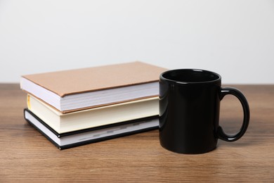 Photo of Black ceramic mug and stack of books on wooden table
