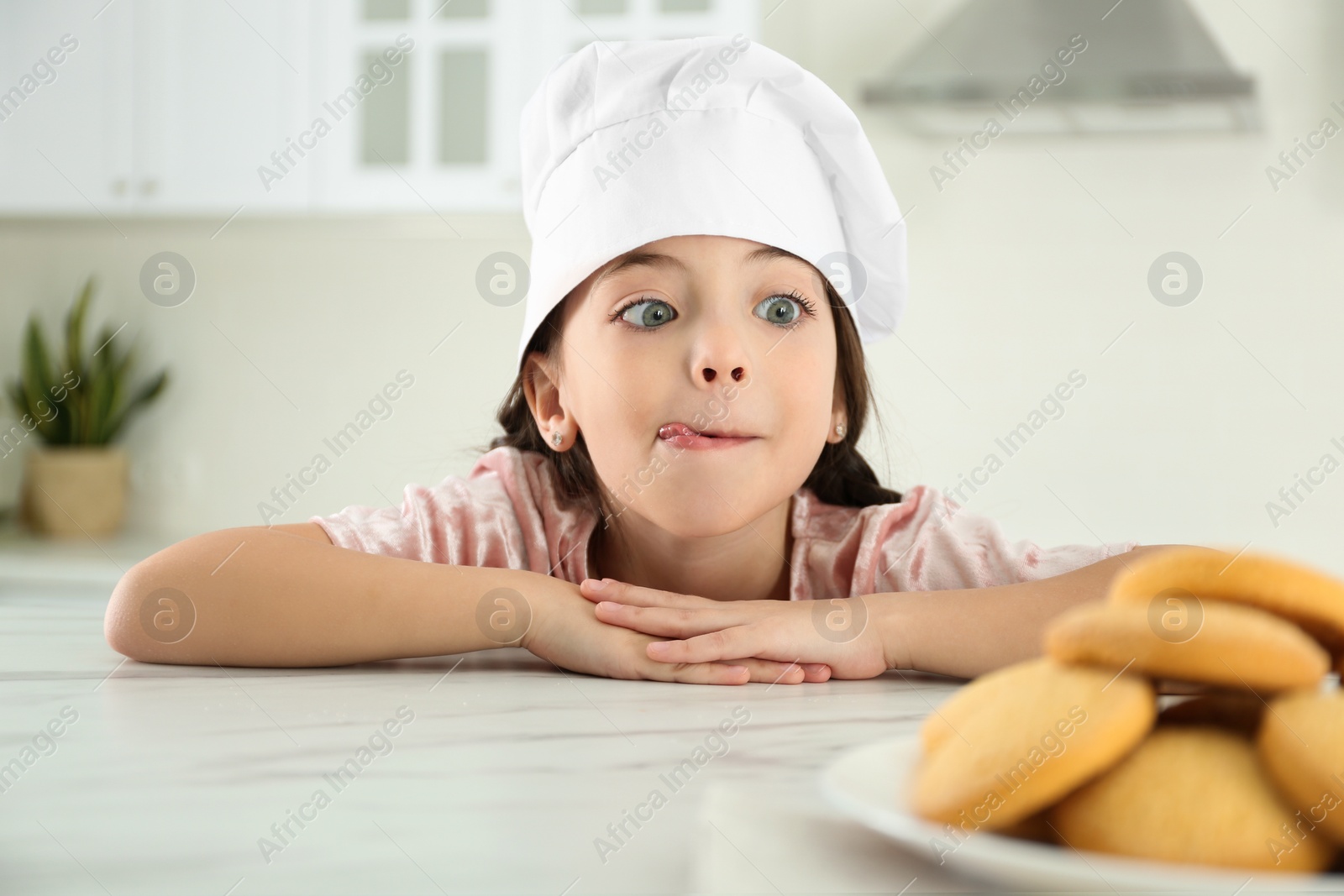 Photo of Cute little girl wearing chef hat at table in kitchen