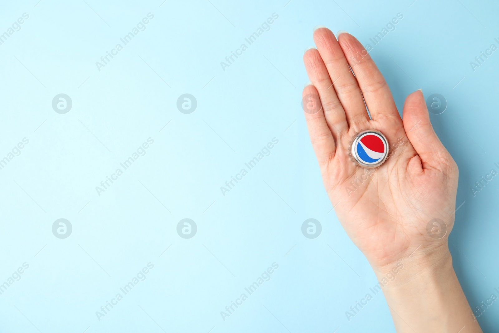 Photo of MYKOLAIV, UKRAINE - FEBRUARY 12, 2021: Woman holding Pepsi lid on light blue background, top view. Space for text