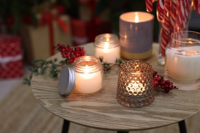 Photo of Burning candles on wooden table near pile of Christmas gifts