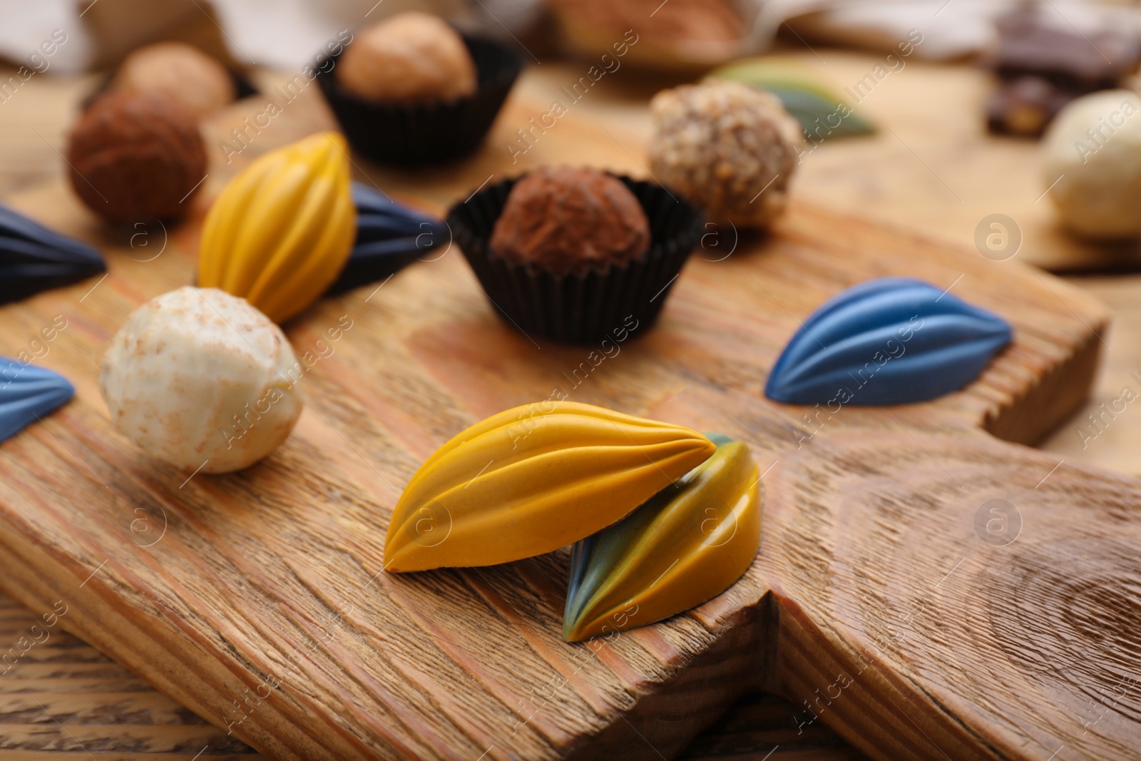 Photo of Different tasty chocolate candies on wooden board, closeup
