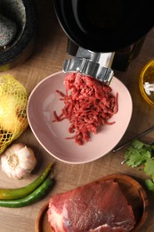 Mincing beef with electric meat grinder on wooden table, flat lay