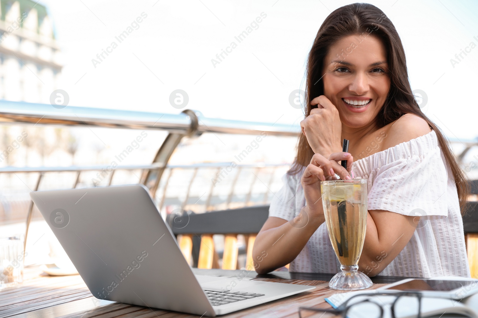 Photo of Beautiful woman with refreshing drink and laptop at outdoor cafe