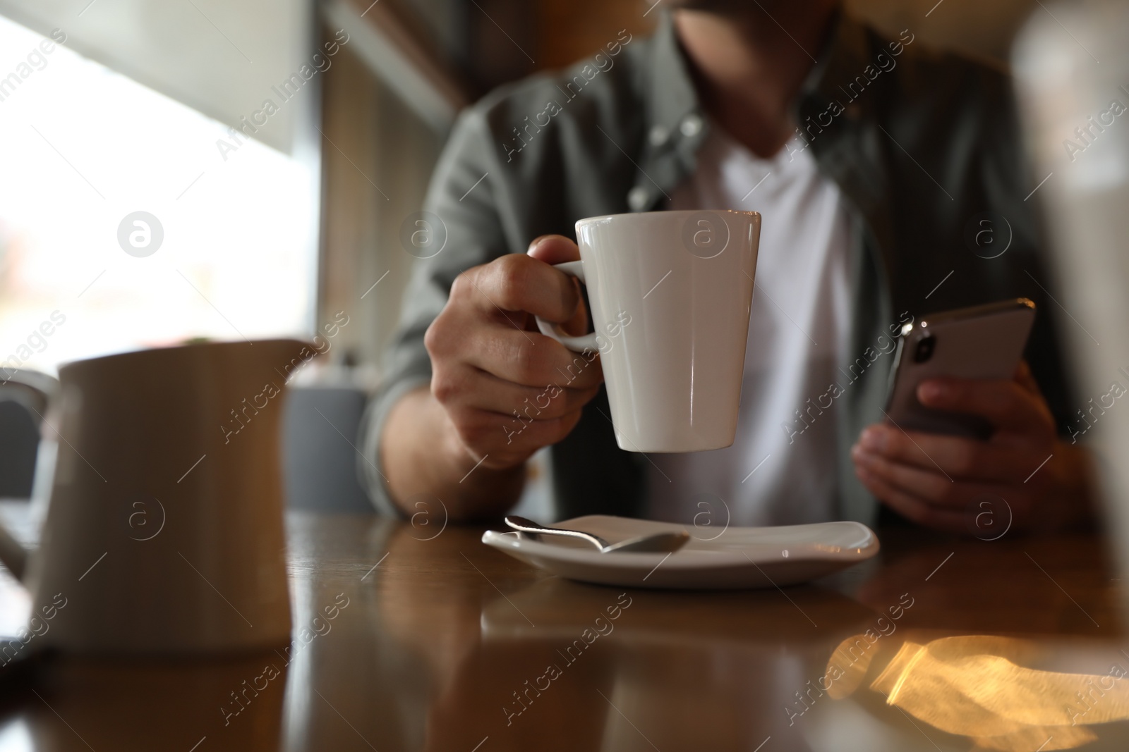 Photo of Man with cup of coffee and smartphone at table in morning, closeup