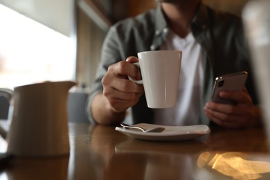 Photo of Man with cup of coffee and smartphone at table in morning, closeup