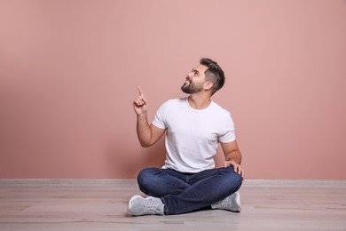 Young man sitting on floor near pink wall indoors