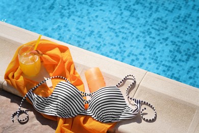 Glass of refreshing drink and different beach accessories near outdoor swimming pool on sunny day, above view. Space for text