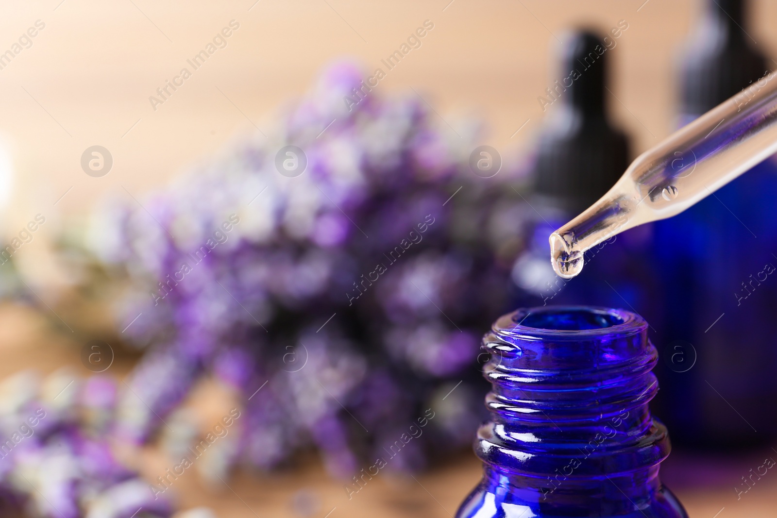 Photo of Dropper with lavender essential oil over bottle on blurred background, closeup. Space for text