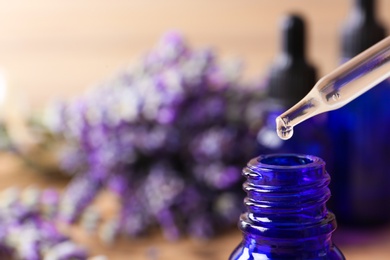 Dropper with lavender essential oil over bottle on blurred background, closeup. Space for text