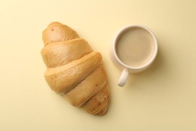 Photo of Delicious fresh croissant and cup of coffee on beige table, flat lay