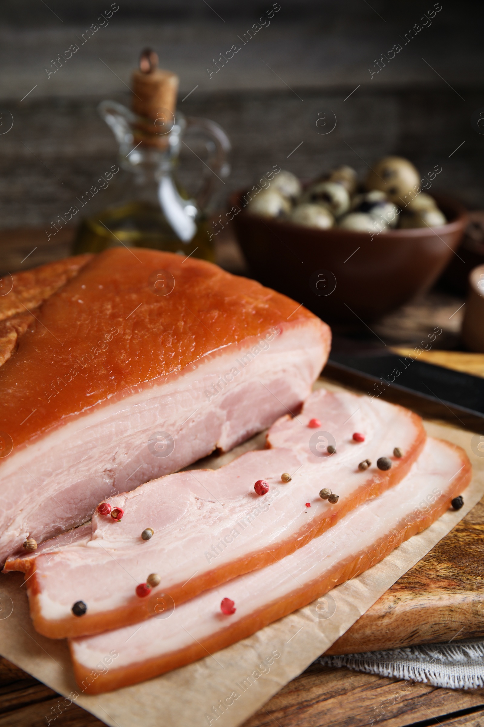 Photo of Delicious smoked bacon with peppercorns on wooden table, closeup