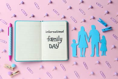 Photo of Happy International Family Day. Flat lay composition with notebook and paper people cutout on pink background