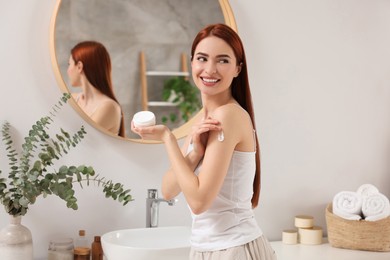 Photo of Beautiful young woman applying body cream onto shoulder in bathroom, space for text