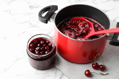 Photo of Pot with cherries in sugar syrup on white marble table. Making delicious jam