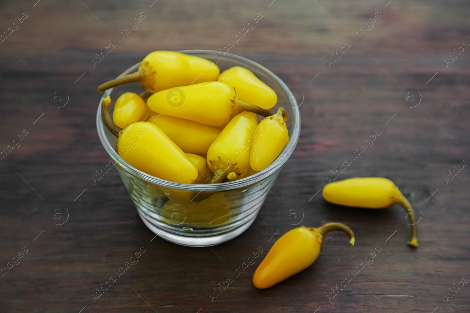 Photo of Glass bowl of pickled yellow jalapeno peppers on wooden table