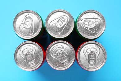 Photo of Energy drinks in wet cans on light blue background, top view