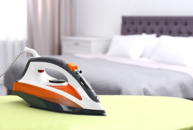 Photo of Modern electric iron on board in bedroom, space for text. Laundry day