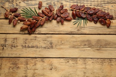 Branches of sweet dried dates with green leaves on wooden table, flat lay. Space for text