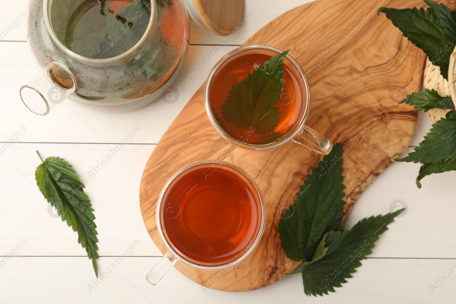 Photo of Aromatic nettle tea and green leaves on white wooden table, flat lay