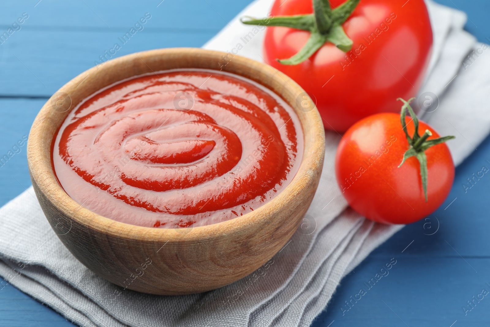 Photo of Bowl of tasty ketchup and tomatoes on blue wooden table, closeup