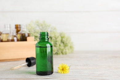 Bottle of essential oil with flower and pipette on wooden table, space for text