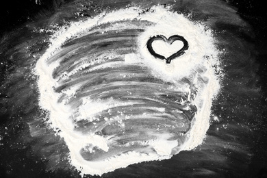 Drawing of heart on flour scattered over black table, top view