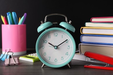 Photo of Alarm clock and different stationery on wooden table near blackboard. School time