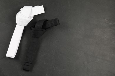 Photo of White and black karate belts on gray background, flat lay. Space for text