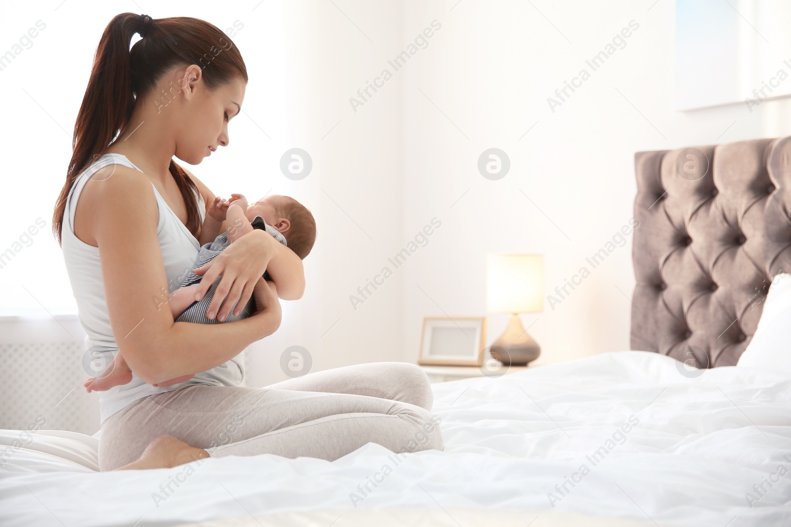 Photo of Young woman holding her baby near breast in bedroom. Space for text