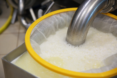 Draining whey from tank into sieve at cheese factory, closeup