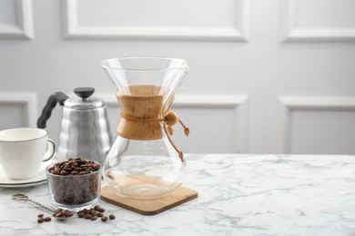 Glass chemex coffeemaker, kettle, beans and cup on white marble table, space for text