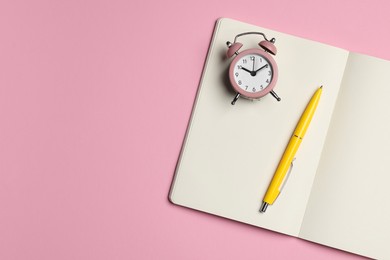 Ballpoint pen, notebook and alarm clock on pink background, top view. Space for text