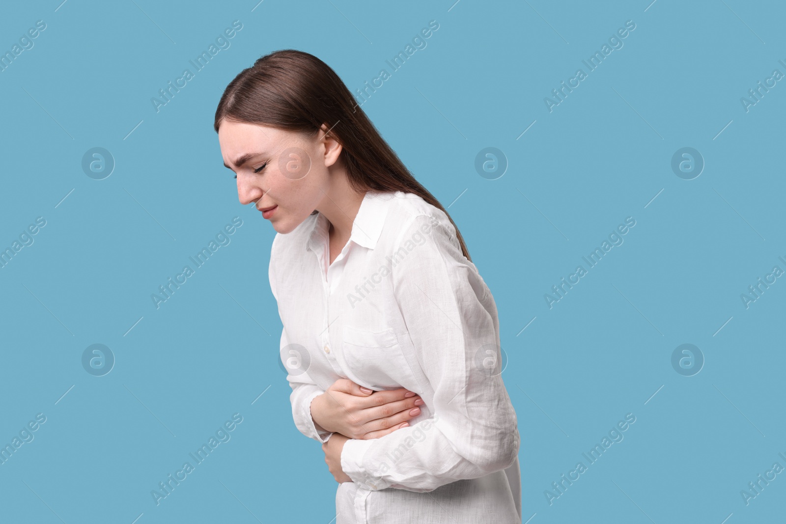 Photo of Young woman suffering from stomach pain on light blue background