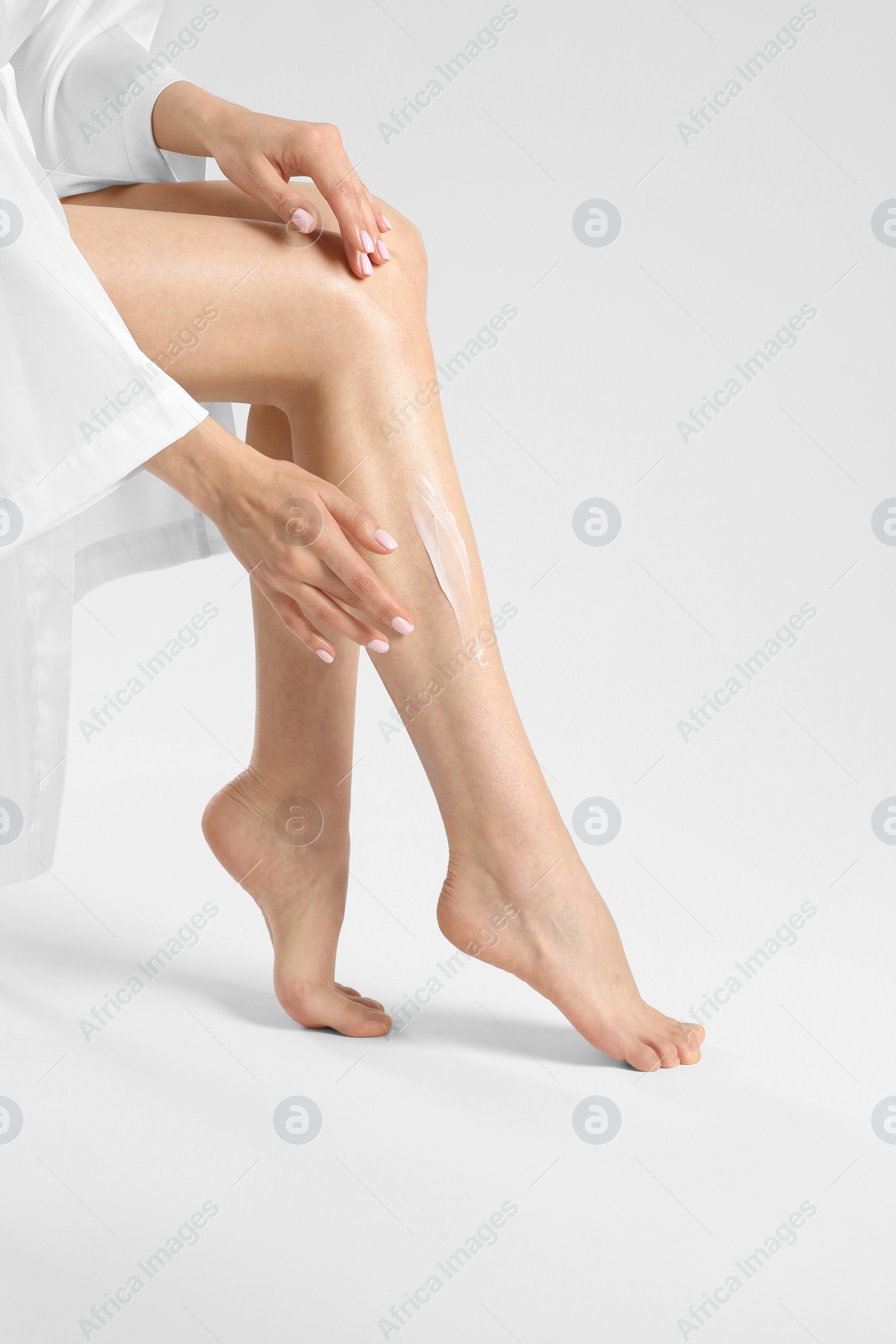 Photo of Woman applying body cream onto her smooth legs on white background, closeup