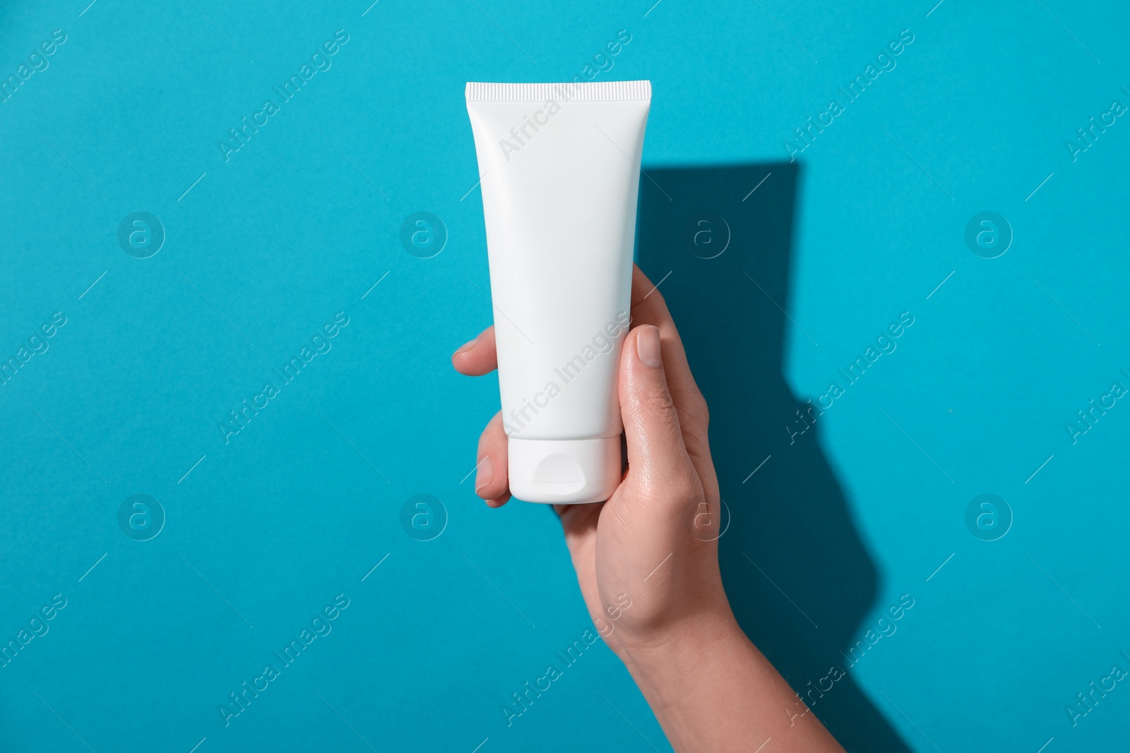 Photo of Woman with tube of hand cream on light blue background, top view