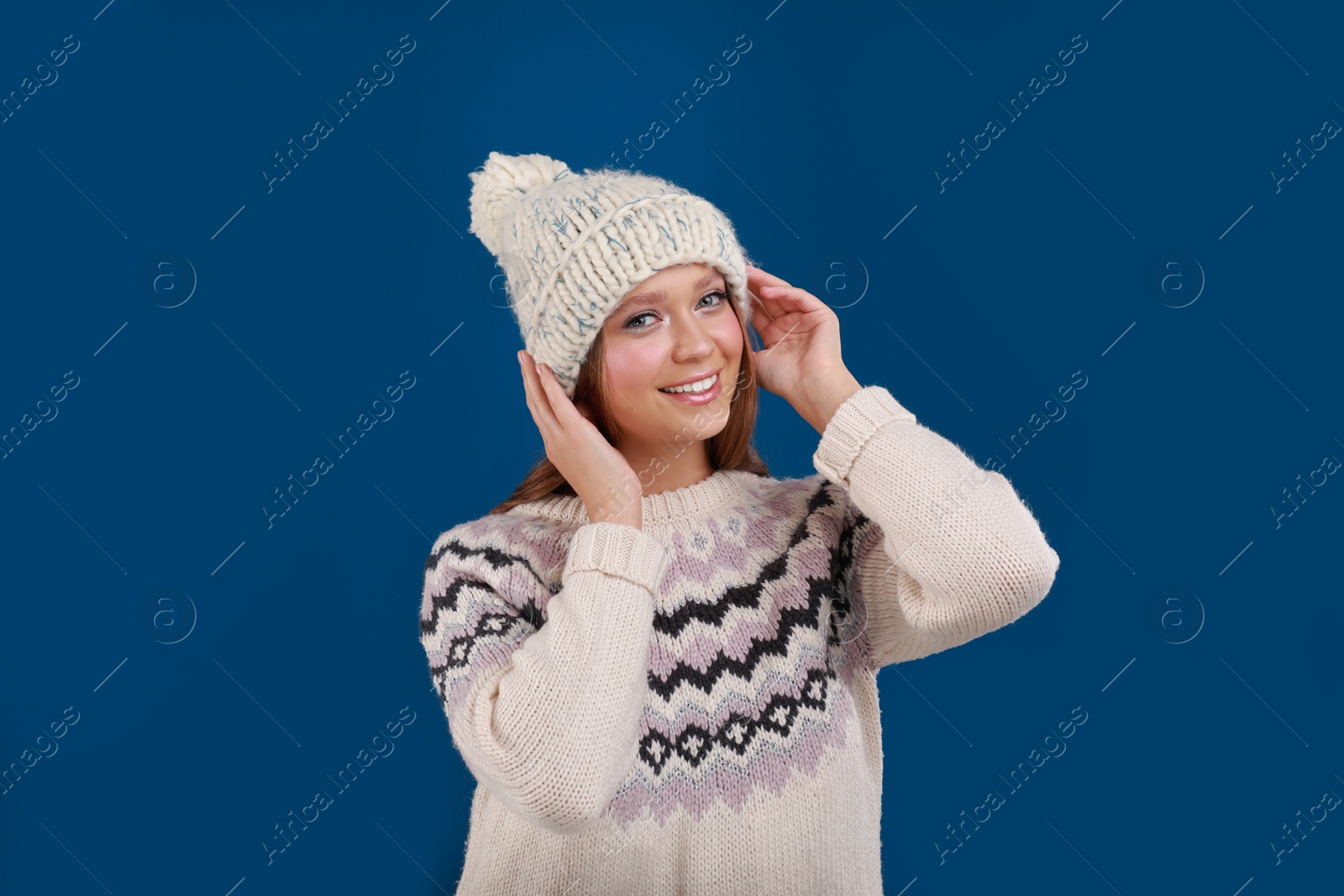 Photo of Young woman in warm sweater and hat on blue background. Winter season