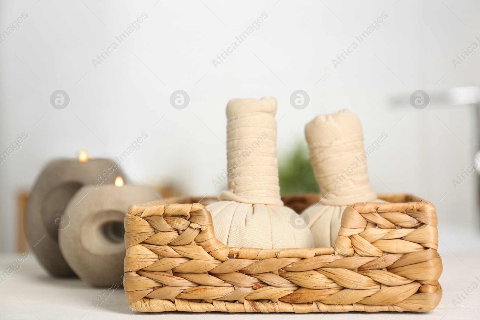 Photo of Burning candles and spa herbal bags on white table in bathroom, closeup