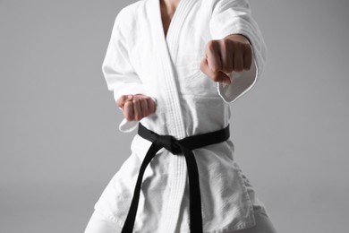 Photo of Martial arts master in keikogi with black belt against grey background, focus on fist