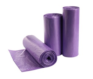 Photo of Rolls of violet garbage bags on white background. Cleaning supplies