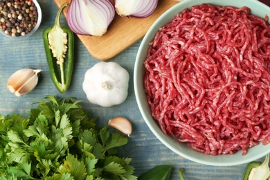 Photo of Flat lay composition with bowl of raw minced meat on blue wooden table