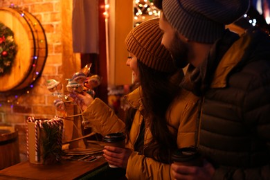 Photo of Lovely couple with cups of hot drinks spending time together at Christmas fair