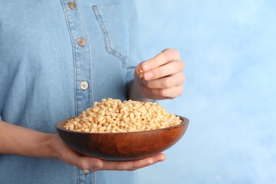 Photo of Woman holding bowl with shelled pine nuts on color background, closeup
