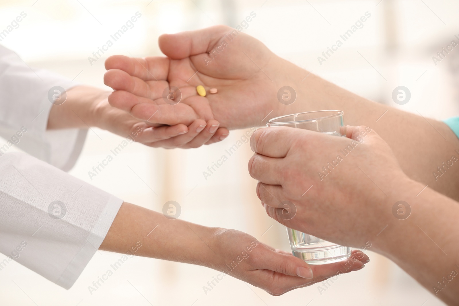 Photo of Nurse giving glass of water and pills to elderly man against blurred background, closeup. Assisting senior generation