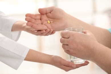 Nurse giving glass of water and pills to elderly man against blurred background, closeup. Assisting senior generation