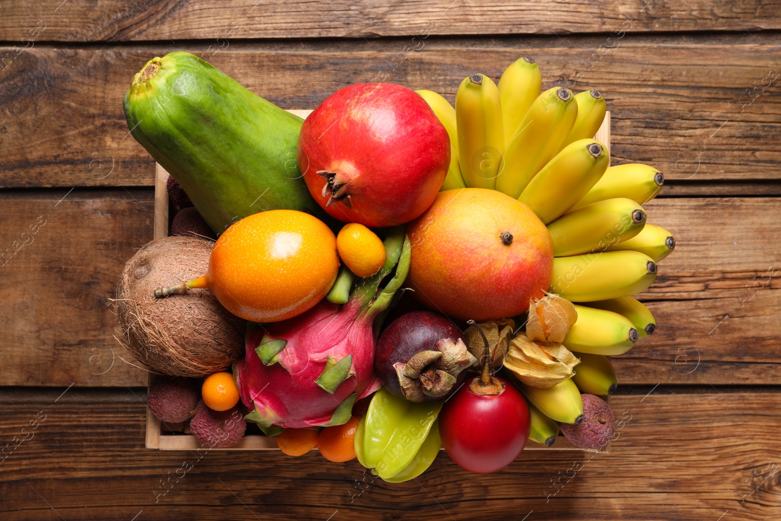 Photo of Crate with different exotic fruits on wooden table, top view